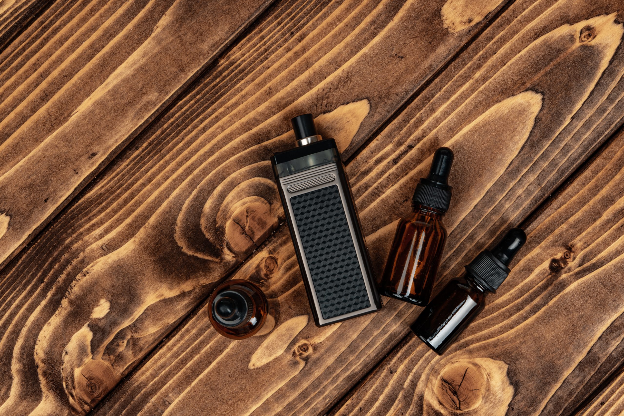 Vape and vape juice bottles on dark brown wooden background